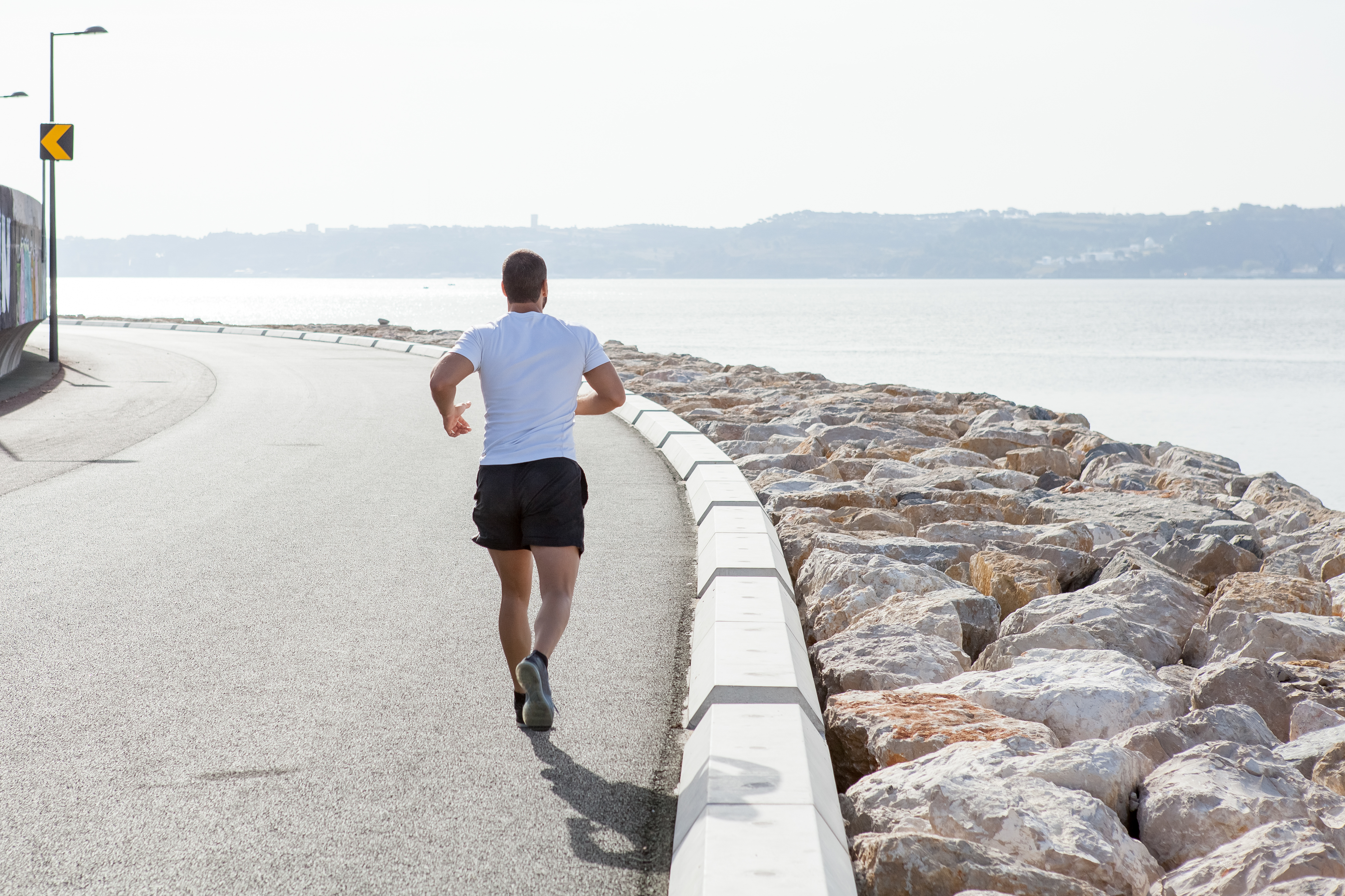 Back view strong man running seaside road