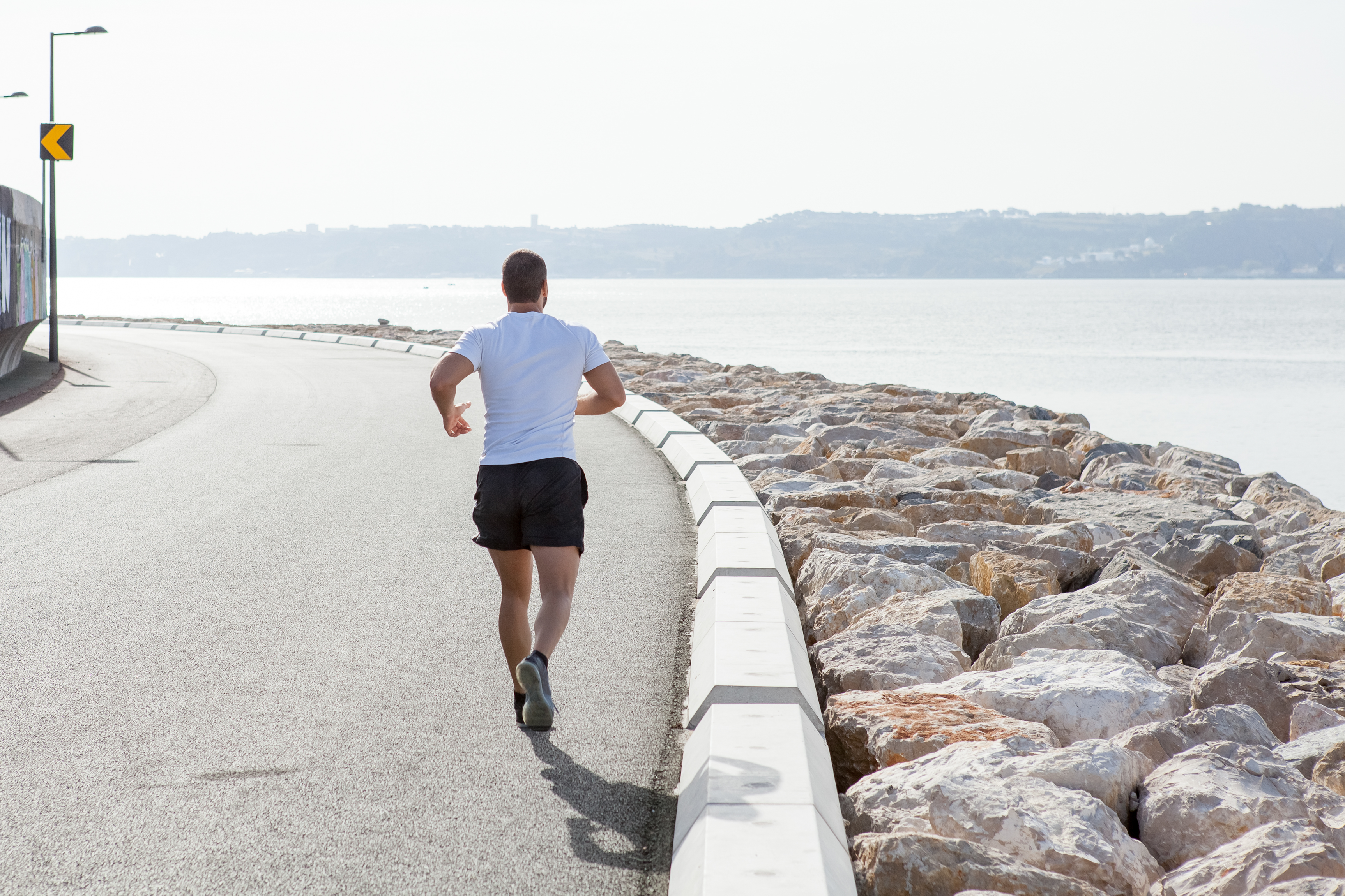 Back view strong man running seaside road