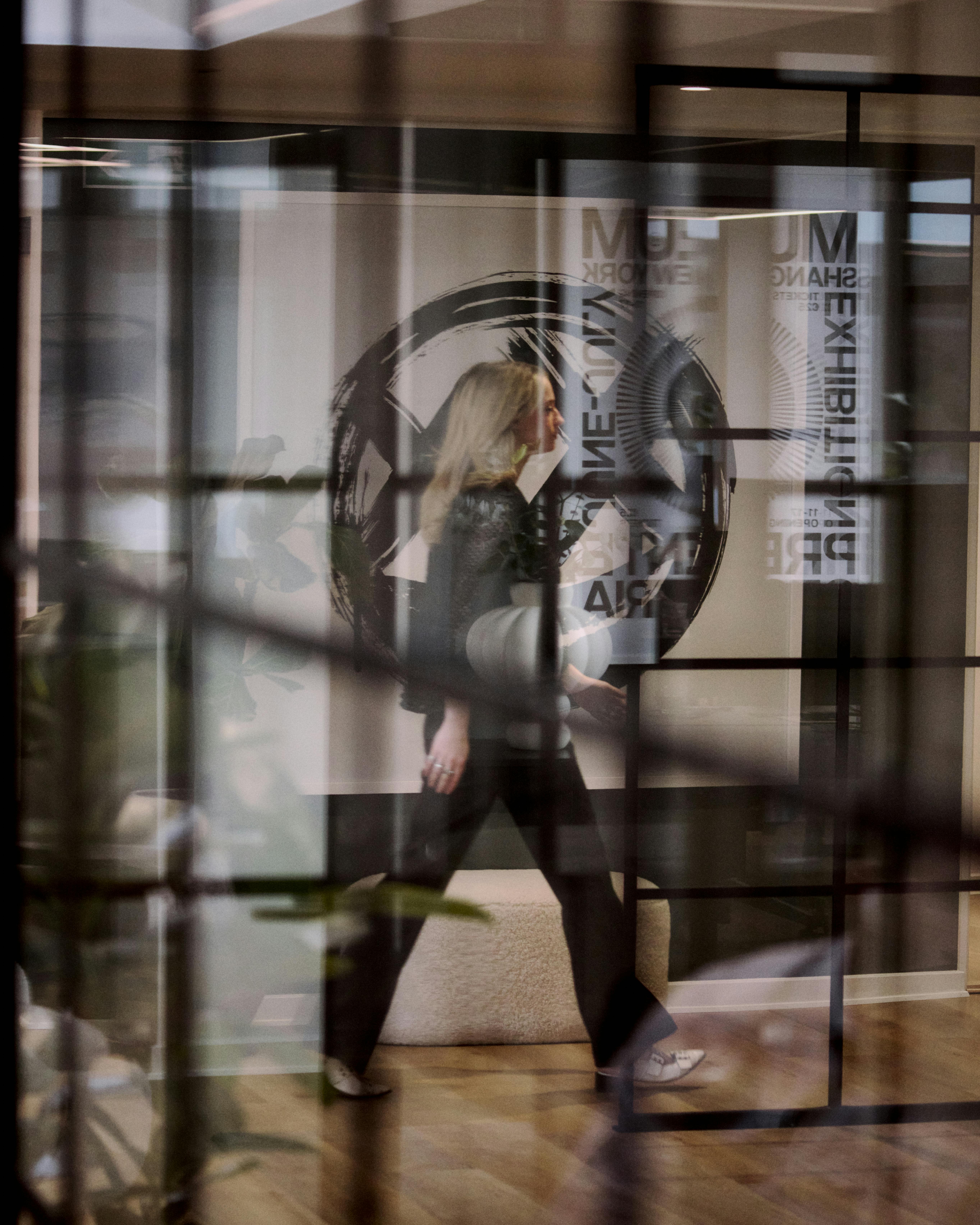 A blond woman walking down a glass corridor
