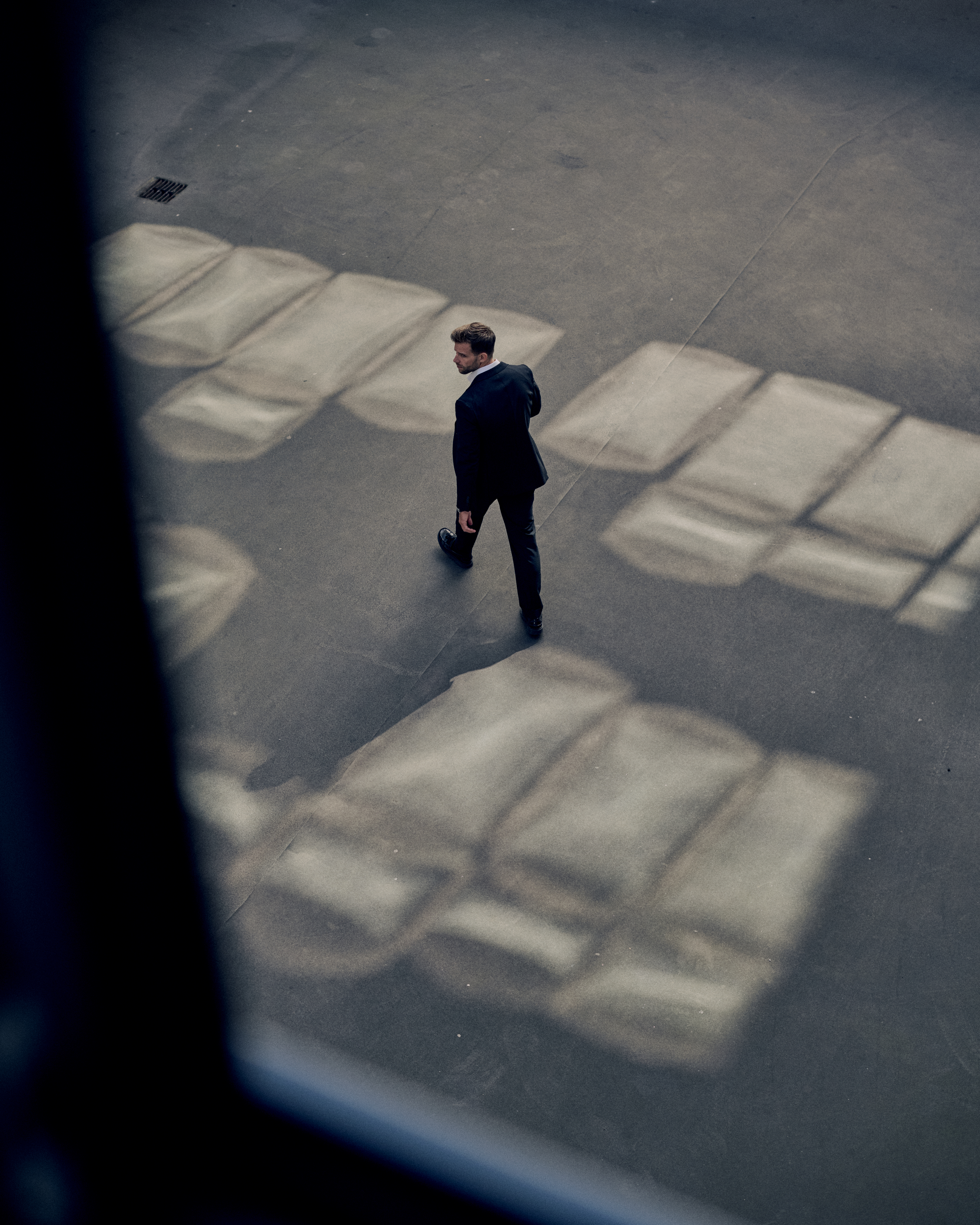 Man walking away in a parking lot, with windows shaping reflections on the ground.