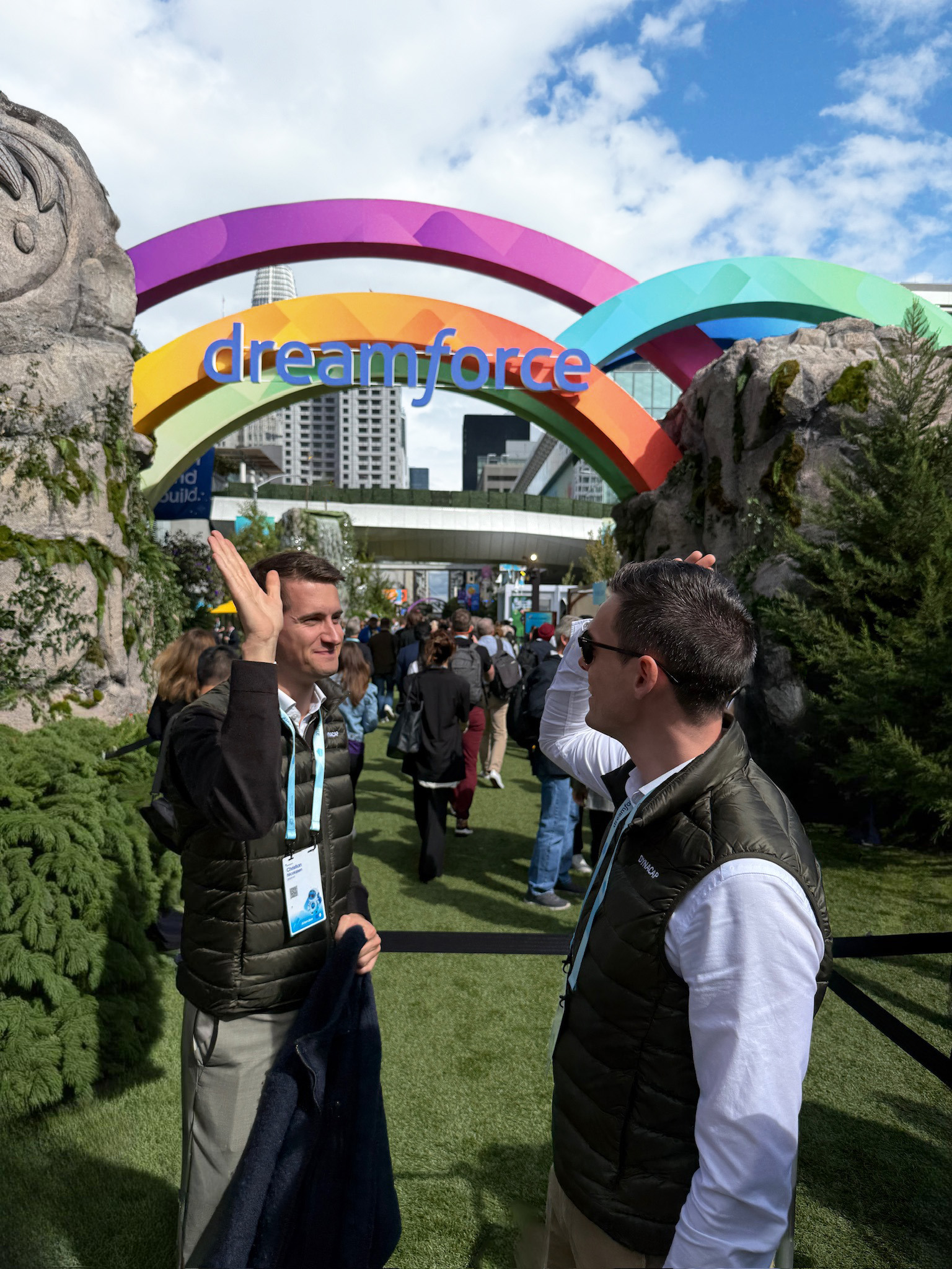 Two men in green vests giving each other high fives in front of Salesforce Dreamforce event.